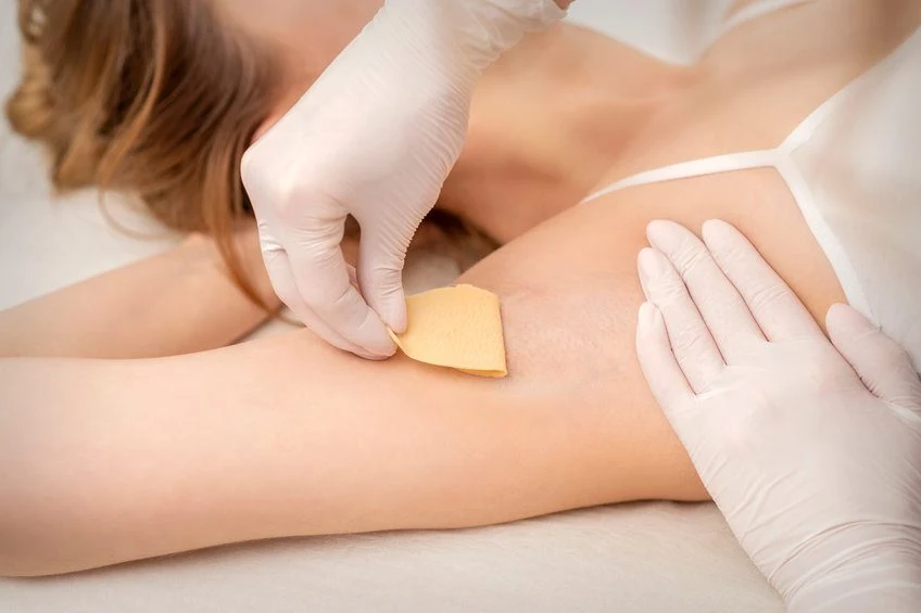 Beautician waxing young female armpit